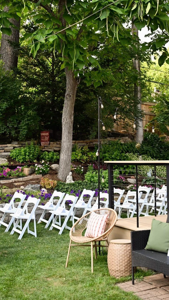 White folding chairs arranged for a ceremony in a lush, landscaped backyard garden.