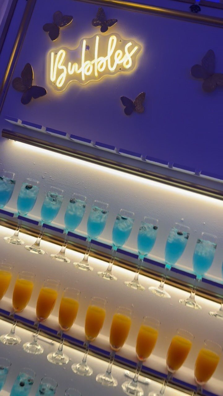 Champagne flutes with blue and orange drinks under a neon Bubbles sign