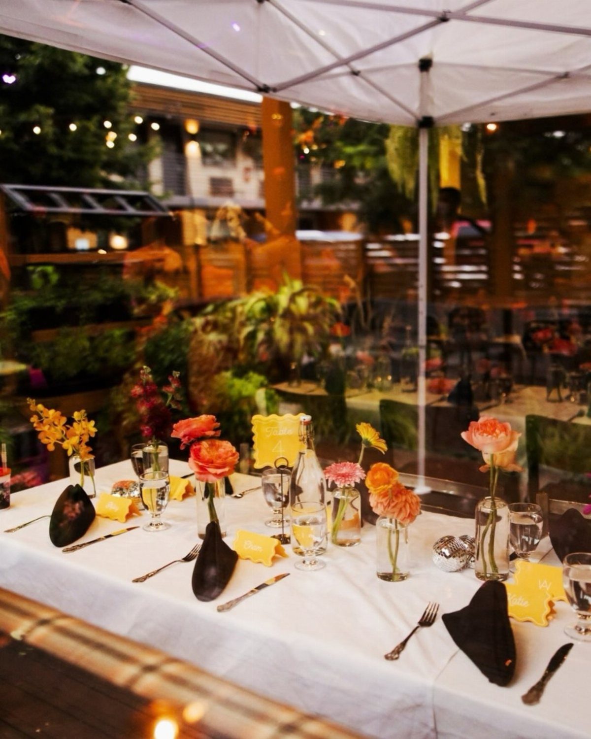 Elegant outdoor dinner table set with white linens and orange floral centerpieces.