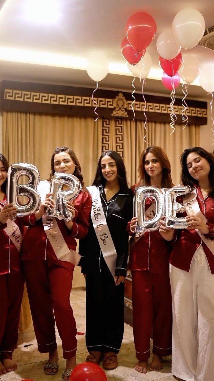 Five women in pajamas posing with silver BRIDE balloons and white bridal sash.