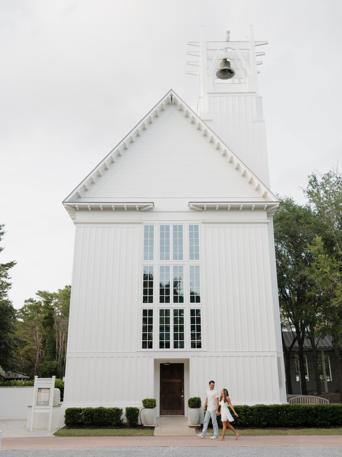 White wooden chapel with a bell tower and a couple walking in front.