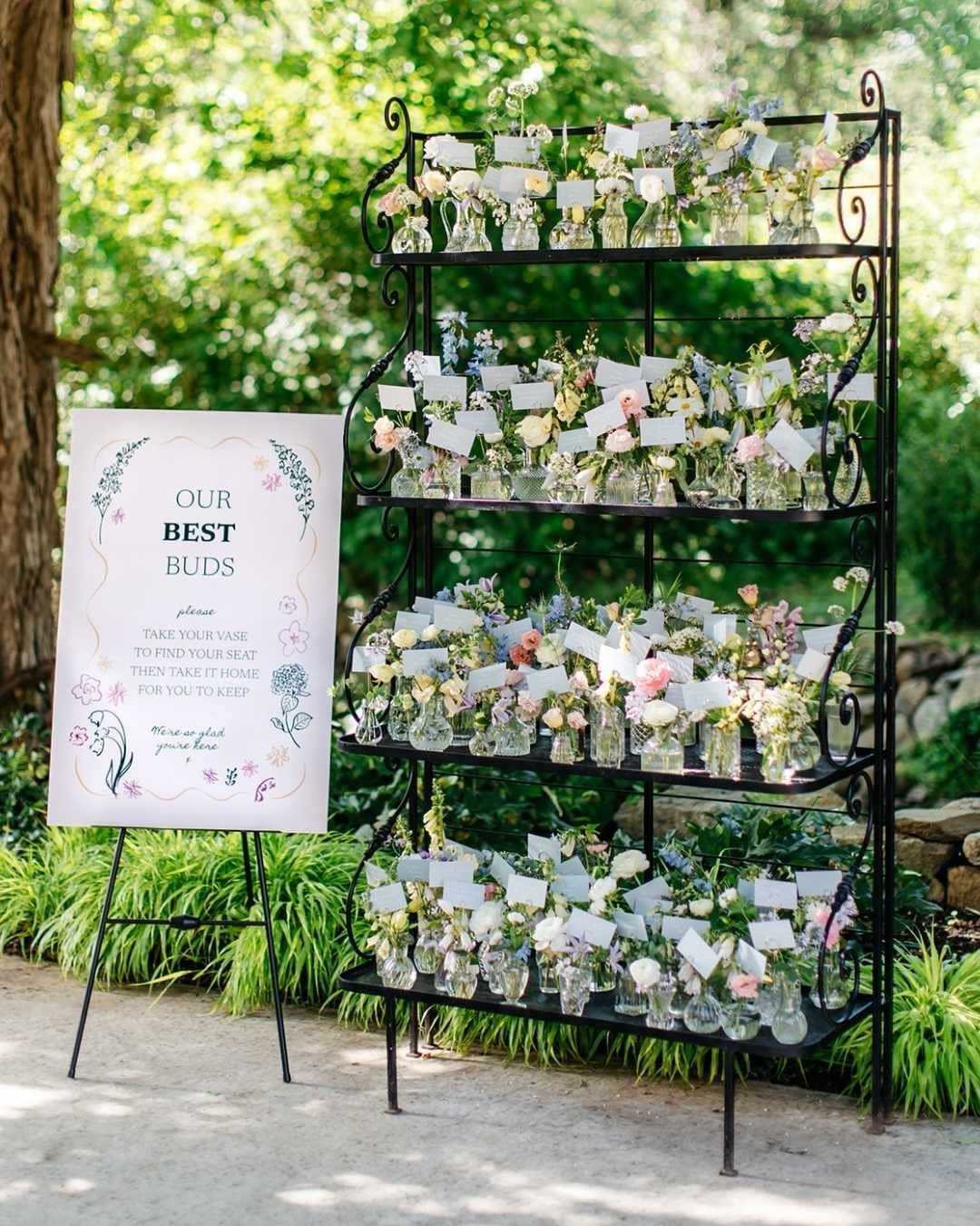 Flower vases with name tags on a black shelf next to a sign.