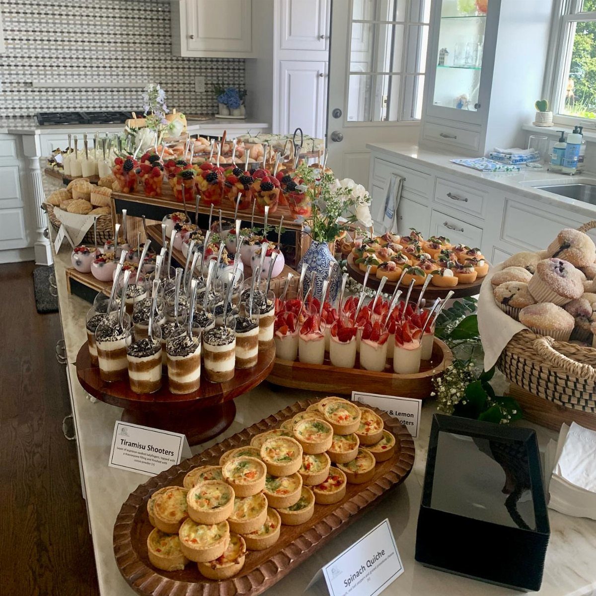 Brunch spread with mini quiches, fruit parfaits, and muffins on a white counter