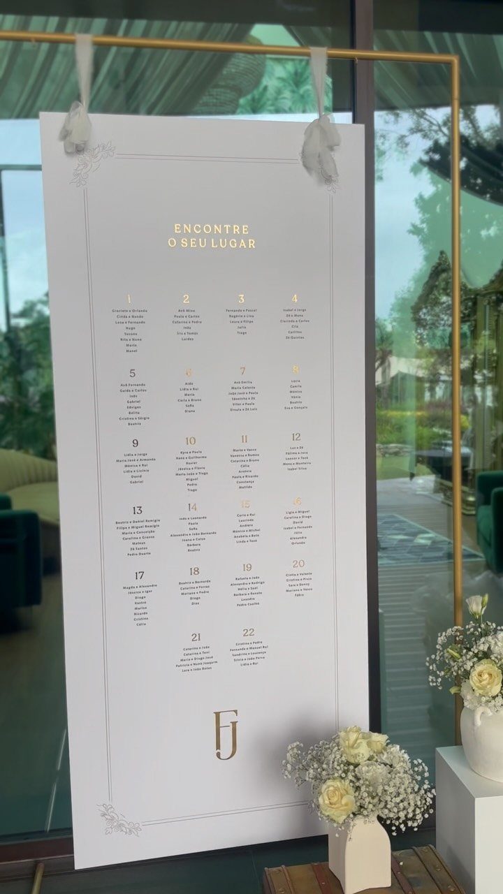 White wedding seating chart with gold lettering hanging from a gold metal frame.