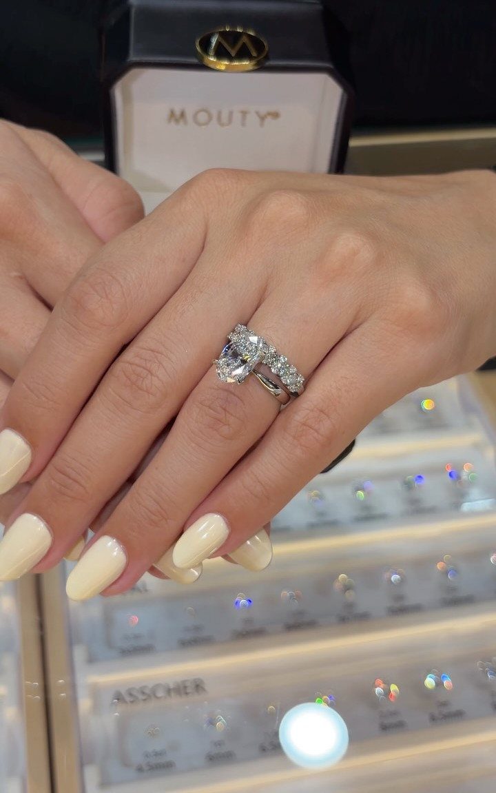 Hand wearing a diamond engagement ring and wedding band over a jewelry display.