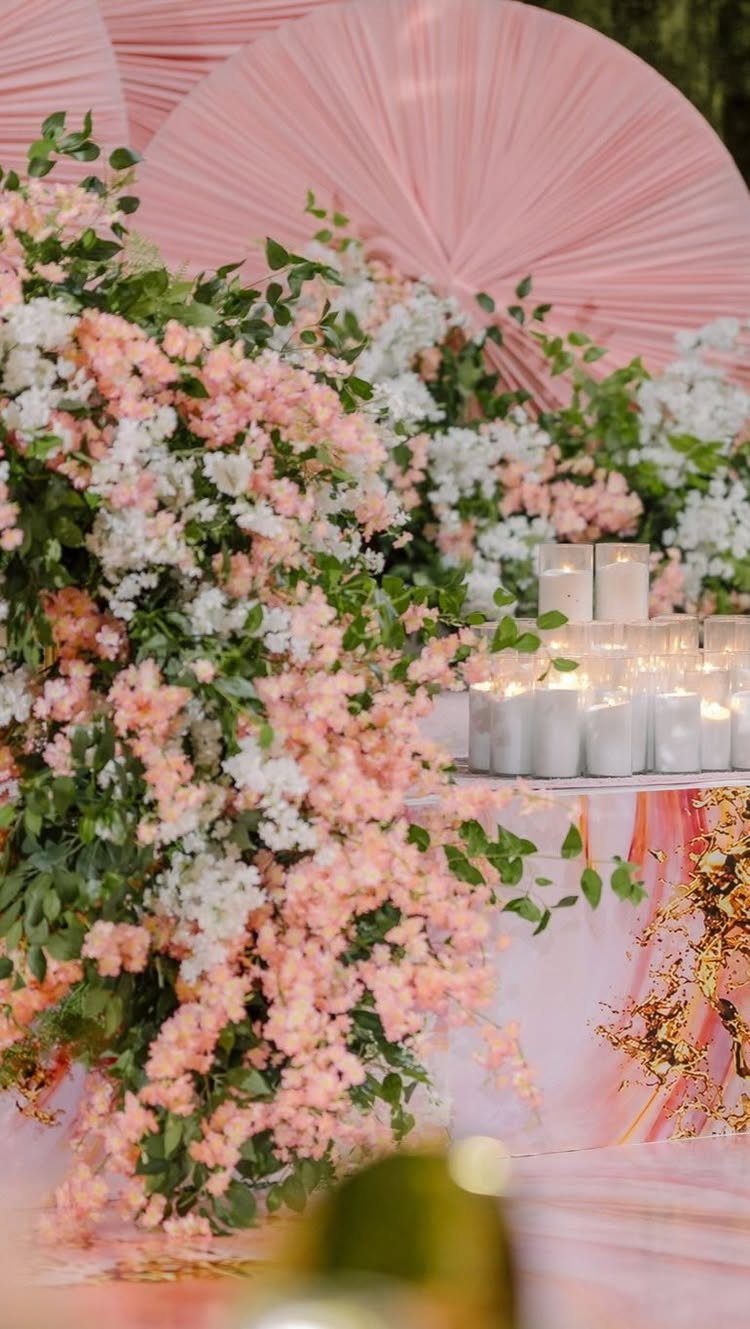 Pink and white floral arrangements with lit candles and a pleated pink backdrop.