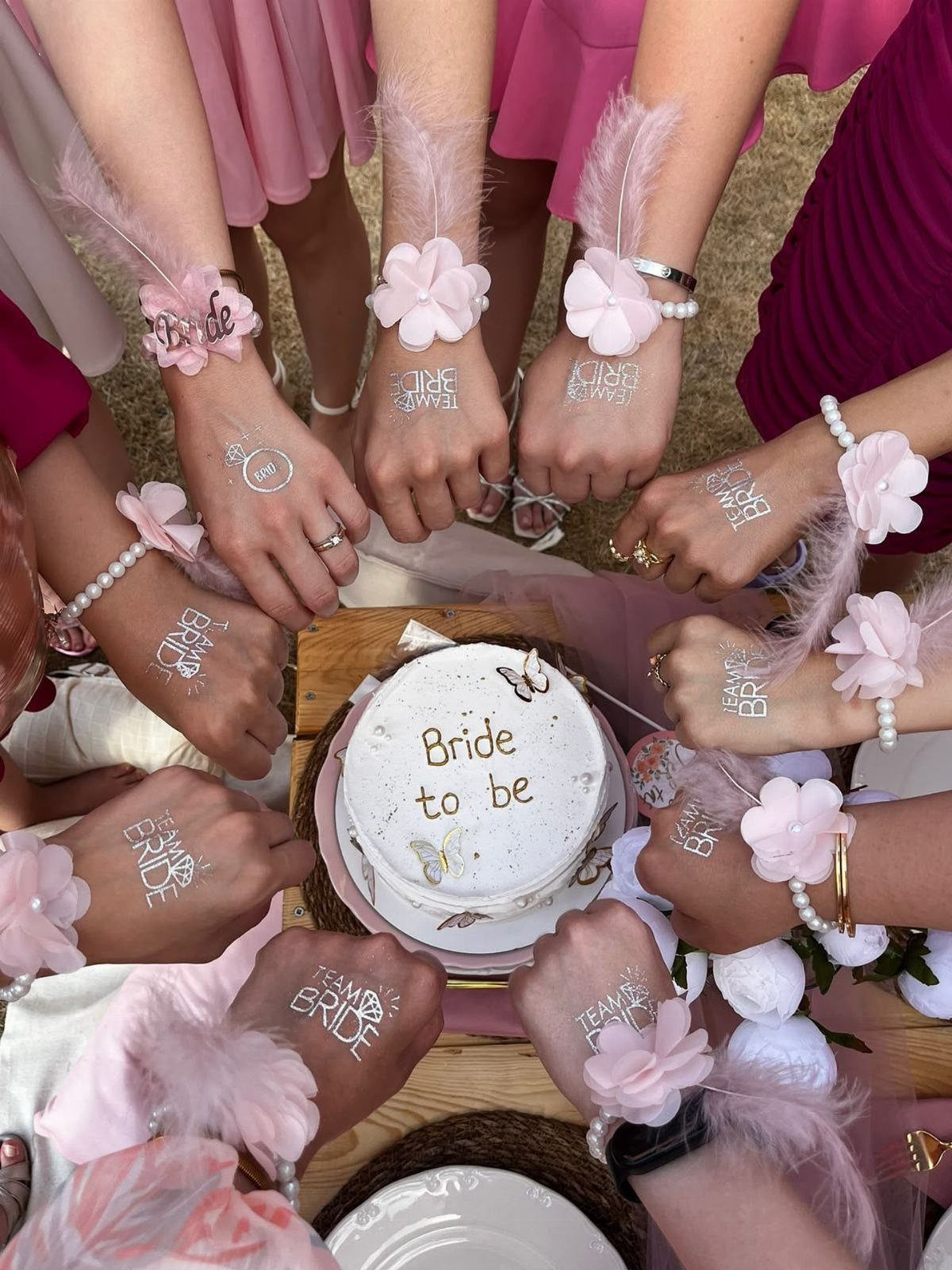 Hands of bridesmaids with Team Bride tattoos surrounding a Bride to be cake