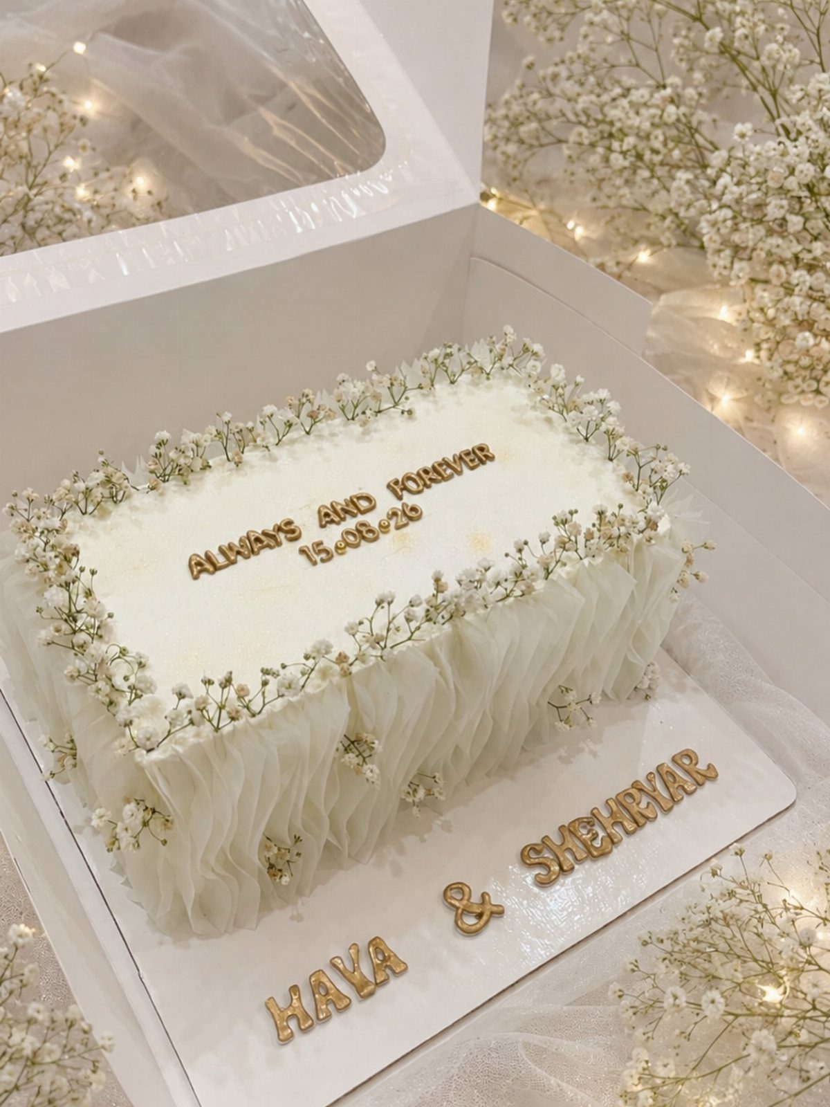 White rectangular wedding cake decorated with baby's breath flowers and gold lettering.