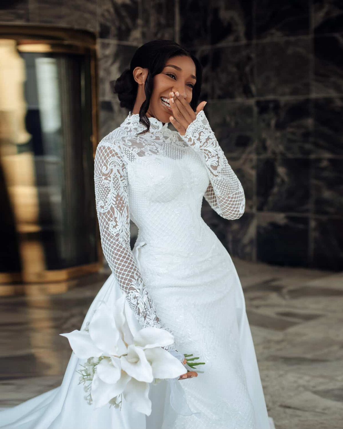 Smiling bride in a high-neck white lace wedding dress holding white lilies.