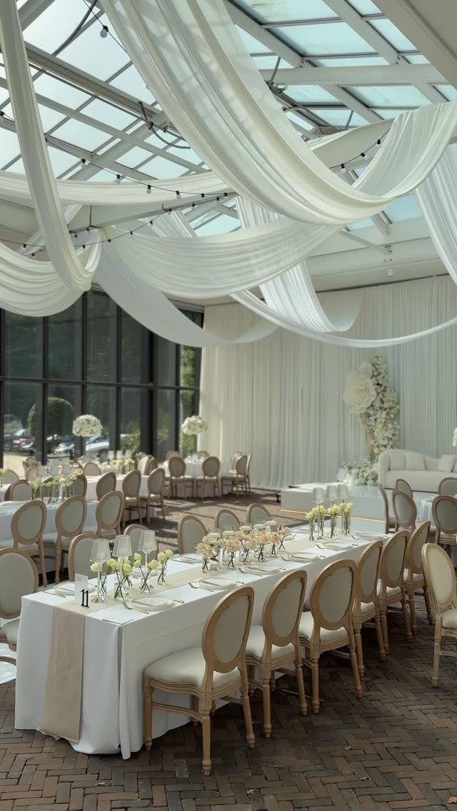 Elegant wedding venue with white fabric draping from a glass ceiling over dining tables.