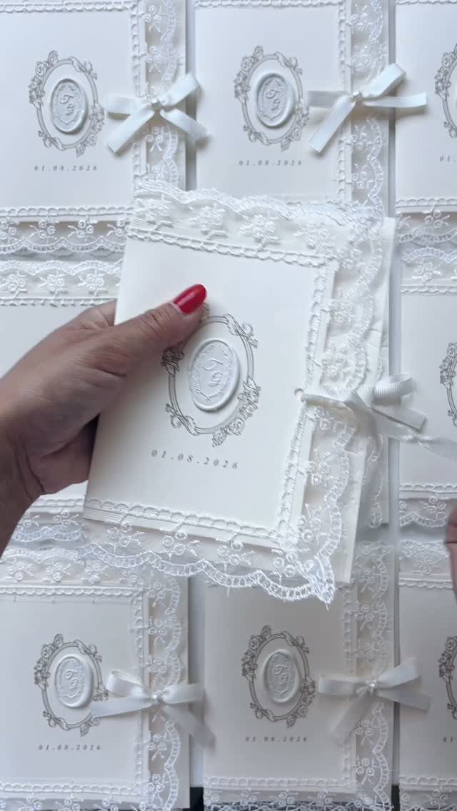 White wedding invitation with a wax seal and ribbon on antique lace fabric.