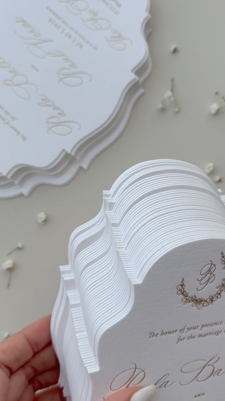 White wedding invitations with scalloped die-cut edges and elegant gold cursive typography.