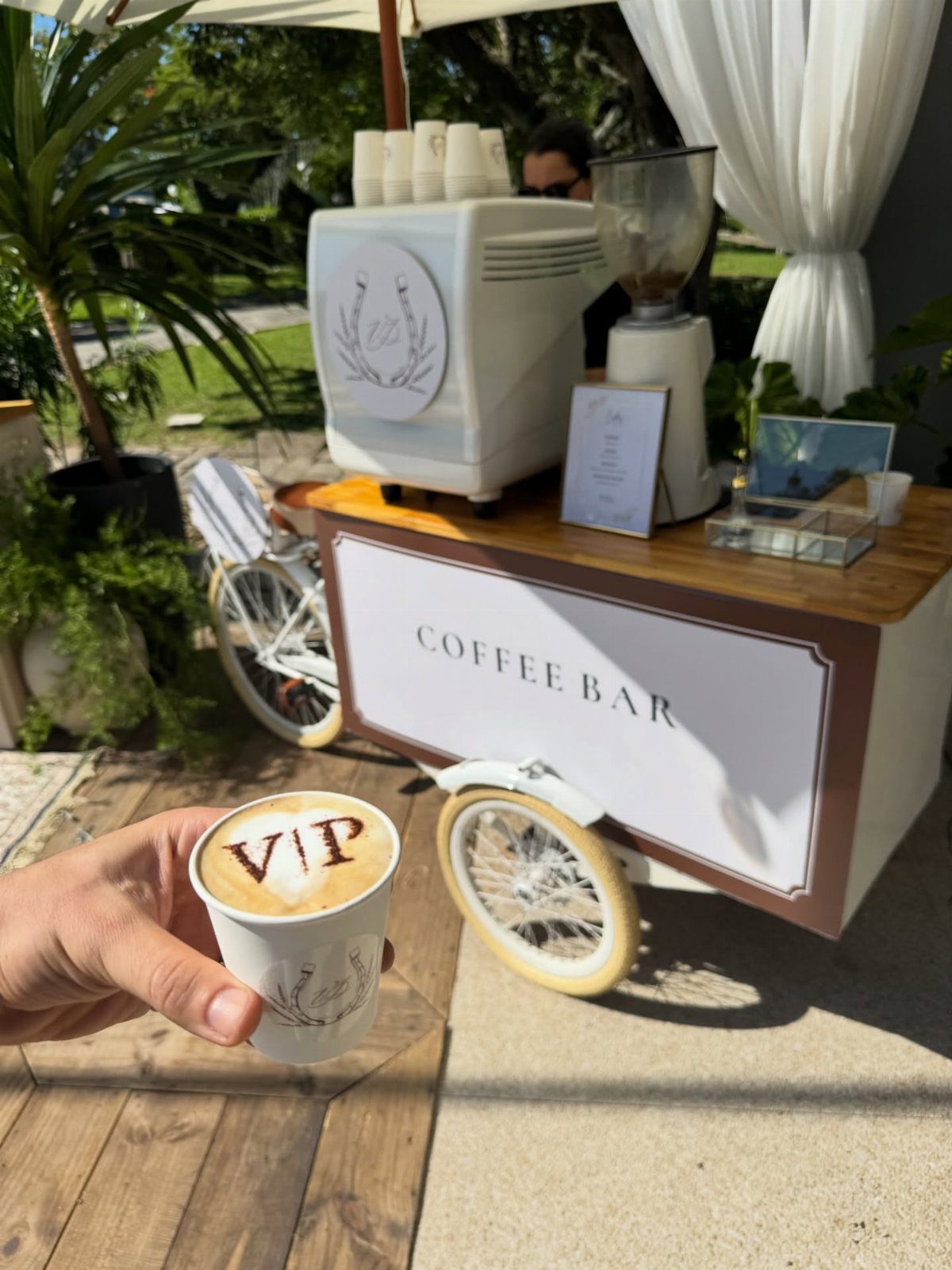 Hand holding a VIP latte in front of a mobile outdoor coffee bar.