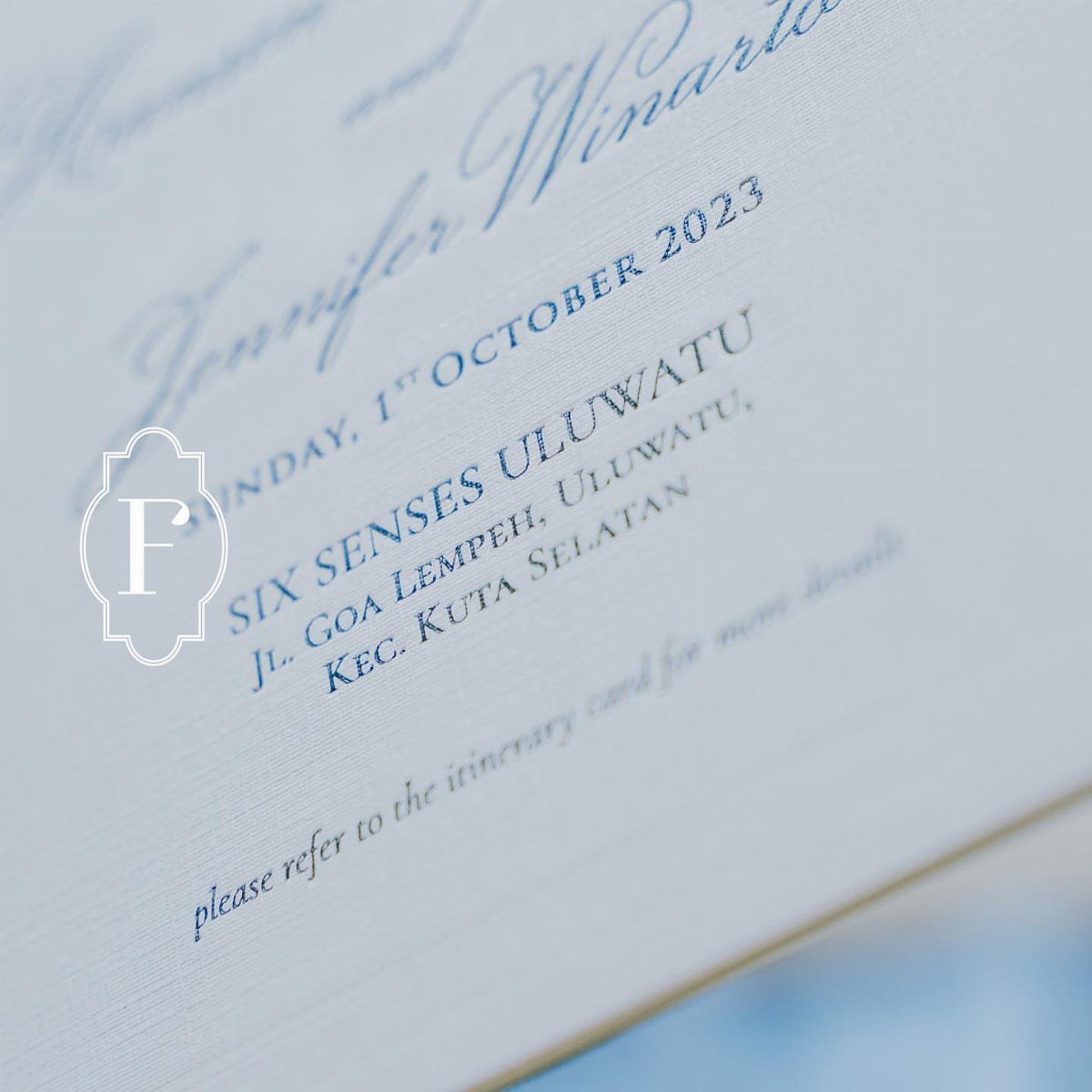 White wedding invitation with elegant blue formal typography and a small crest logo.