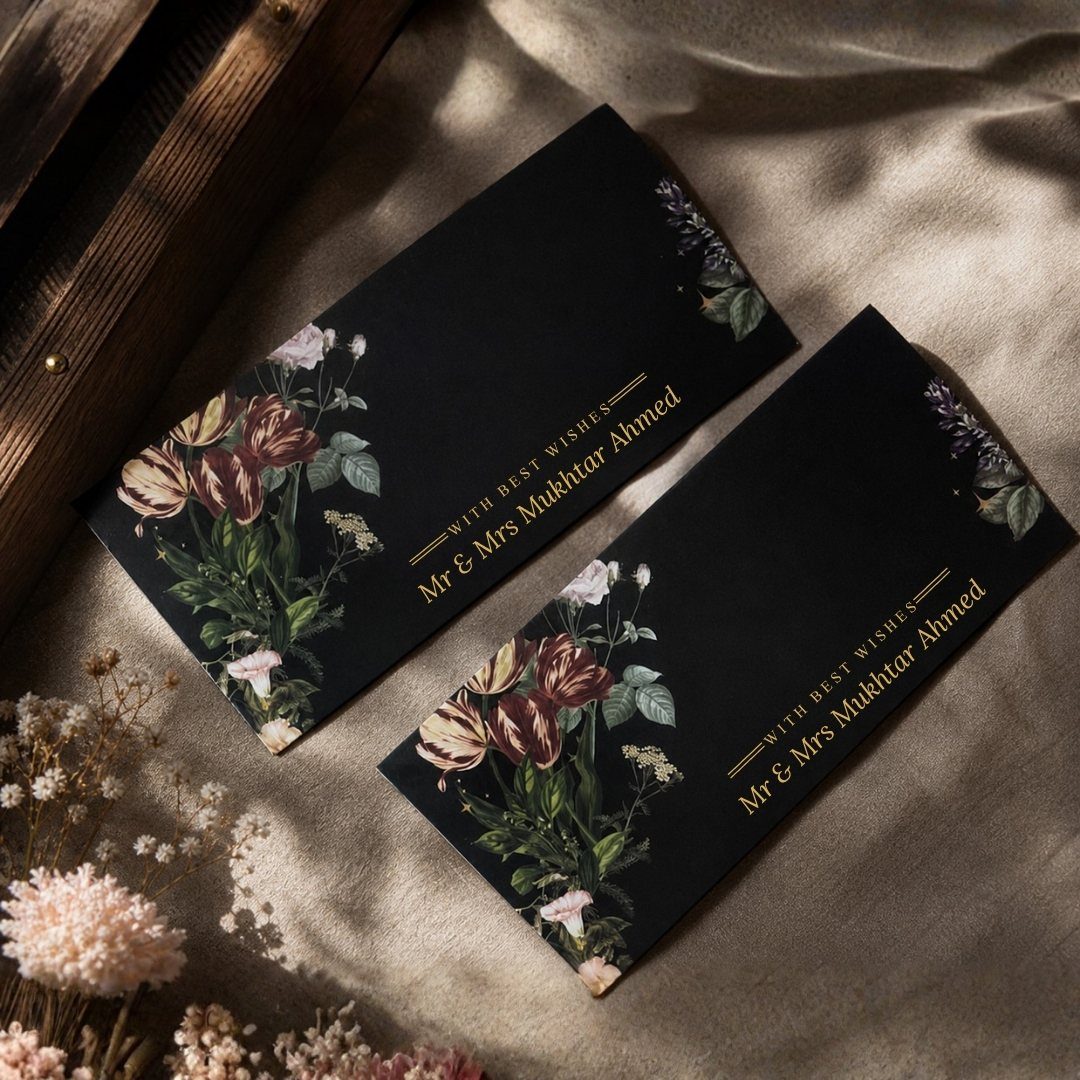 Black wedding invitations with gold lettering and floral illustrations on beige fabric.