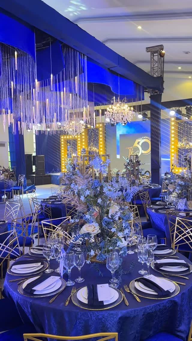 Elegant event hall with blue velvet tables, gold chairs, and floral centerpieces.