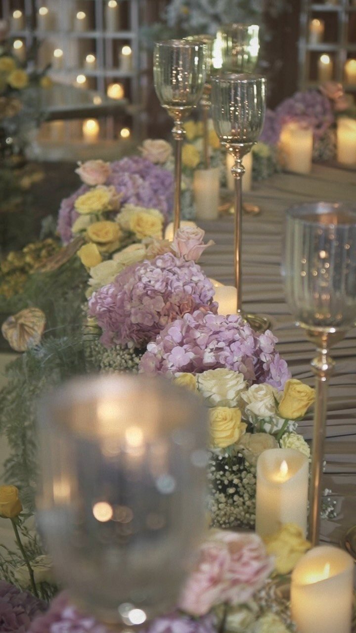 Floral table runner with lit white candles and gold candle holders for an event.