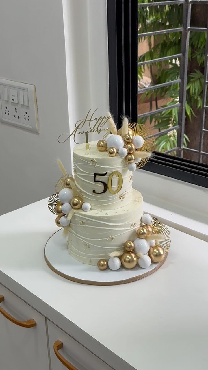 Two-tier white anniversary cake with gold 50 topper and gold sphere decorations.