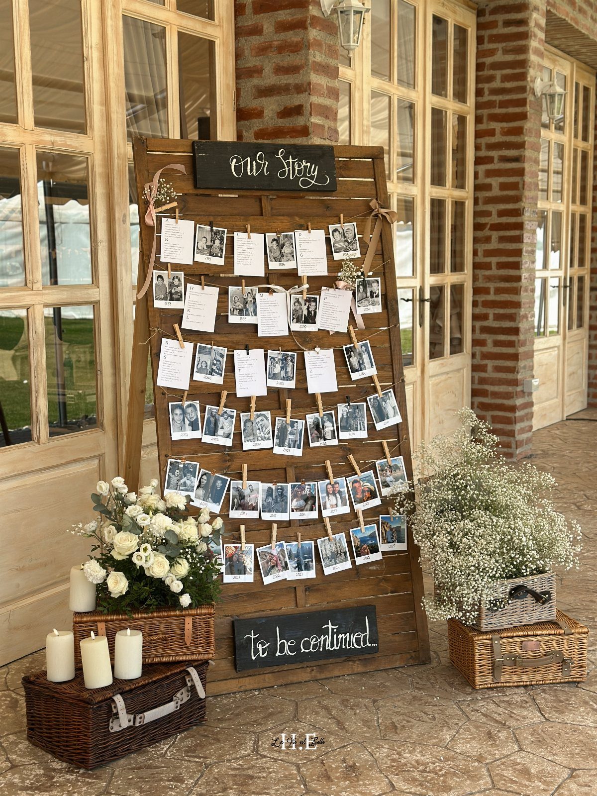 Wooden photo display board with clipped pictures, white flowers, and chalkboards.