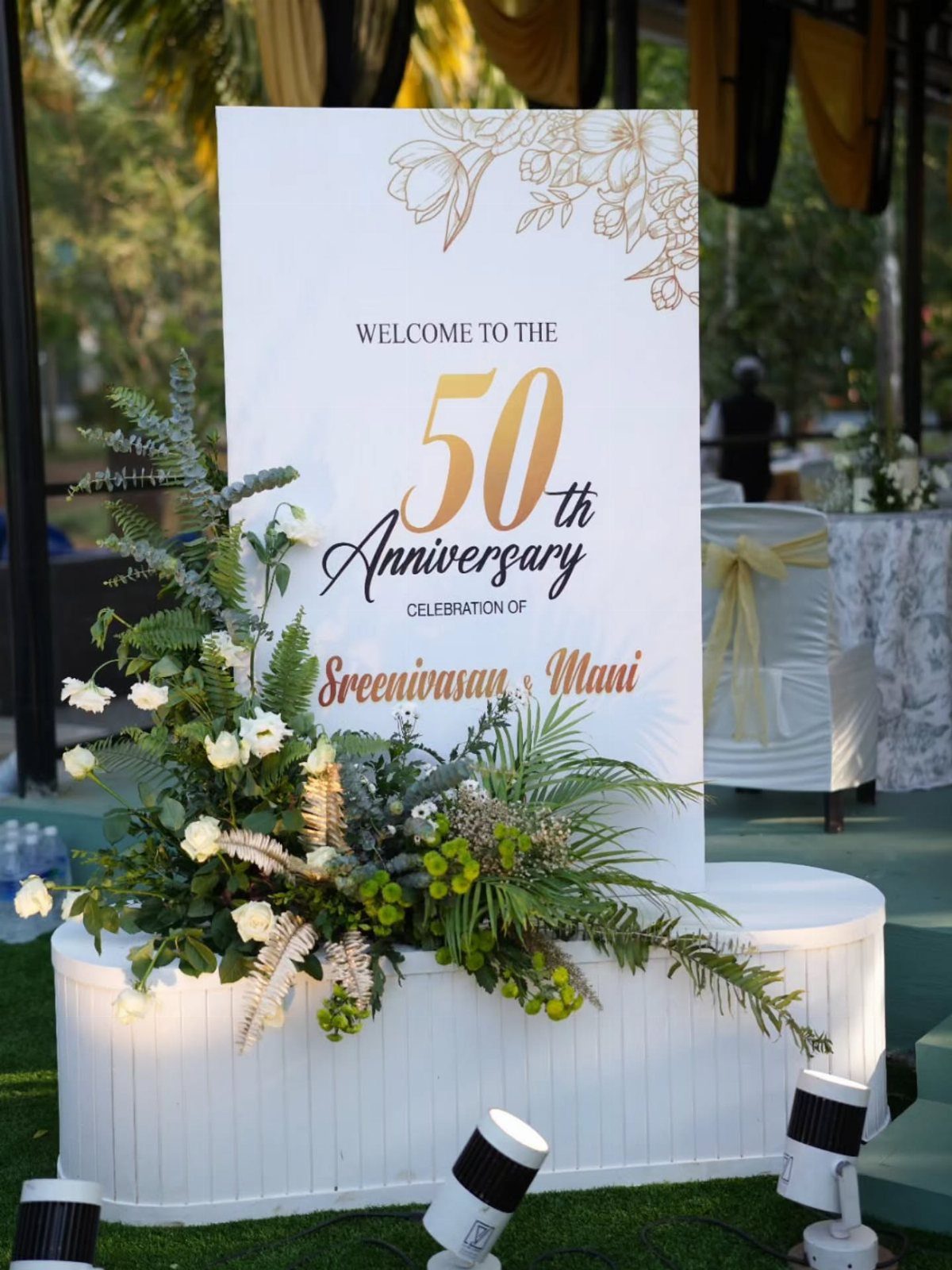 Welcome sign for a 50th anniversary celebration decorated with white flowers and greenery.