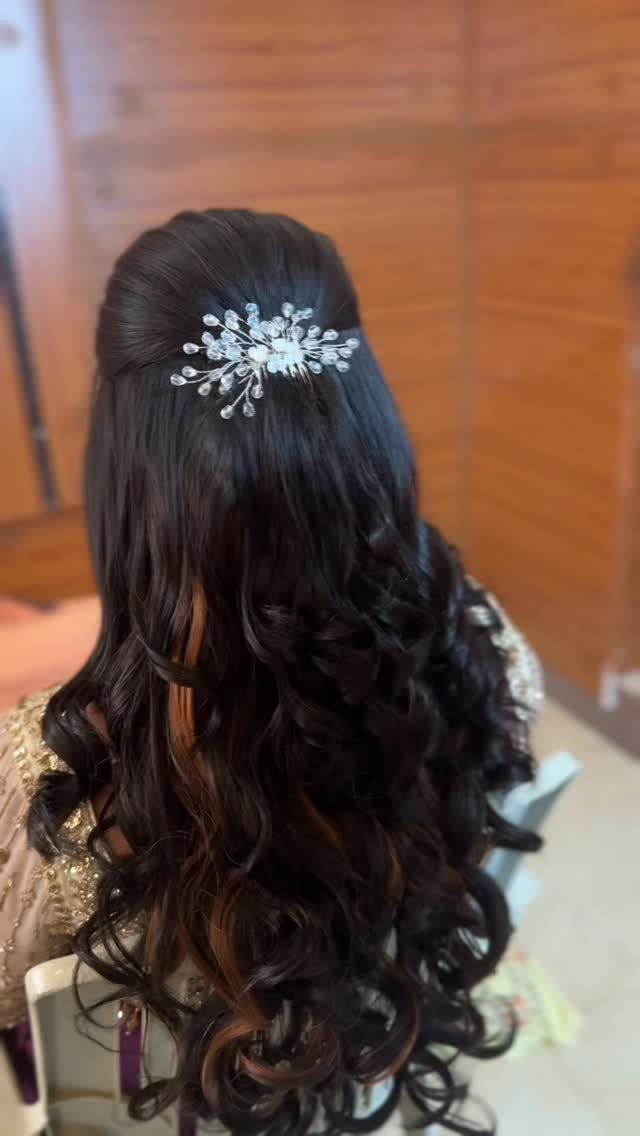 Long dark curly hair styled in a half-updo with a silver floral clip.