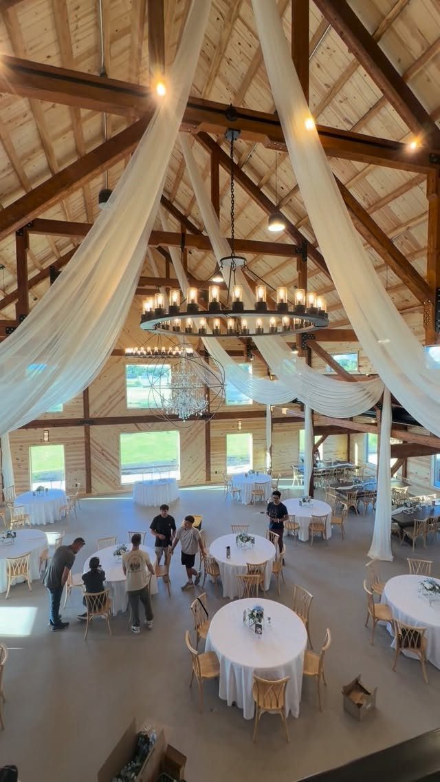 Rustic barn wedding venue with white fabric draping, chandeliers, and set tables.