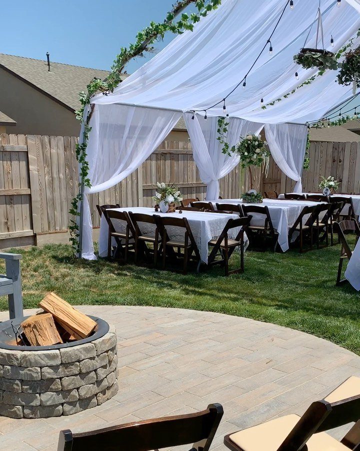White canopy with greenery over dining tables next to a stone fire pit.