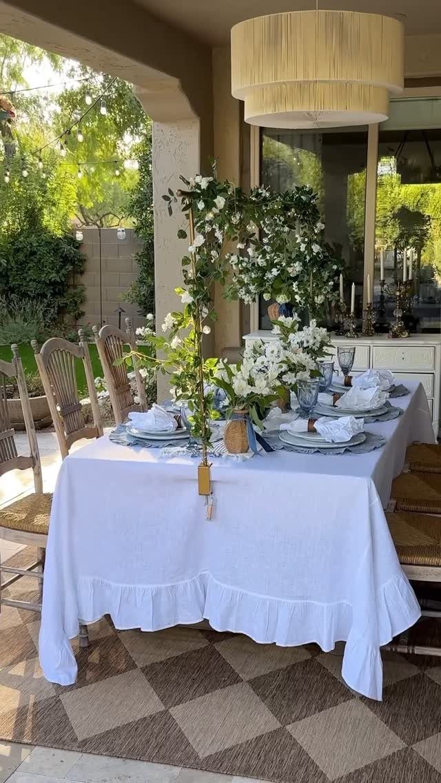 Dining table with white tablecloth and floral arch on a covered backyard patio.