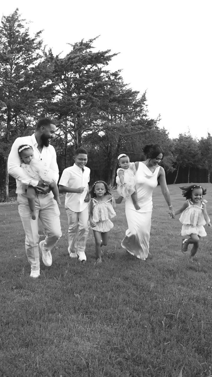A couple and four children walking together across a grassy field in white clothing.