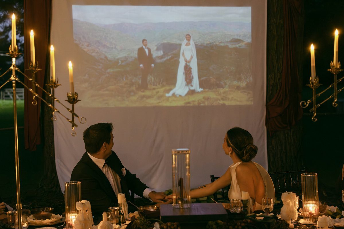 Couple holding hands at a candlelit dinner watching their wedding photo projection.