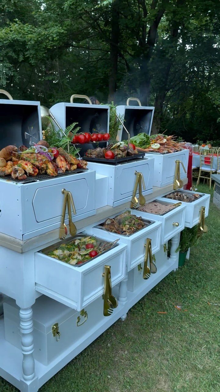 White wooden buffet station with grilled meats and vegetables in an outdoor setting.