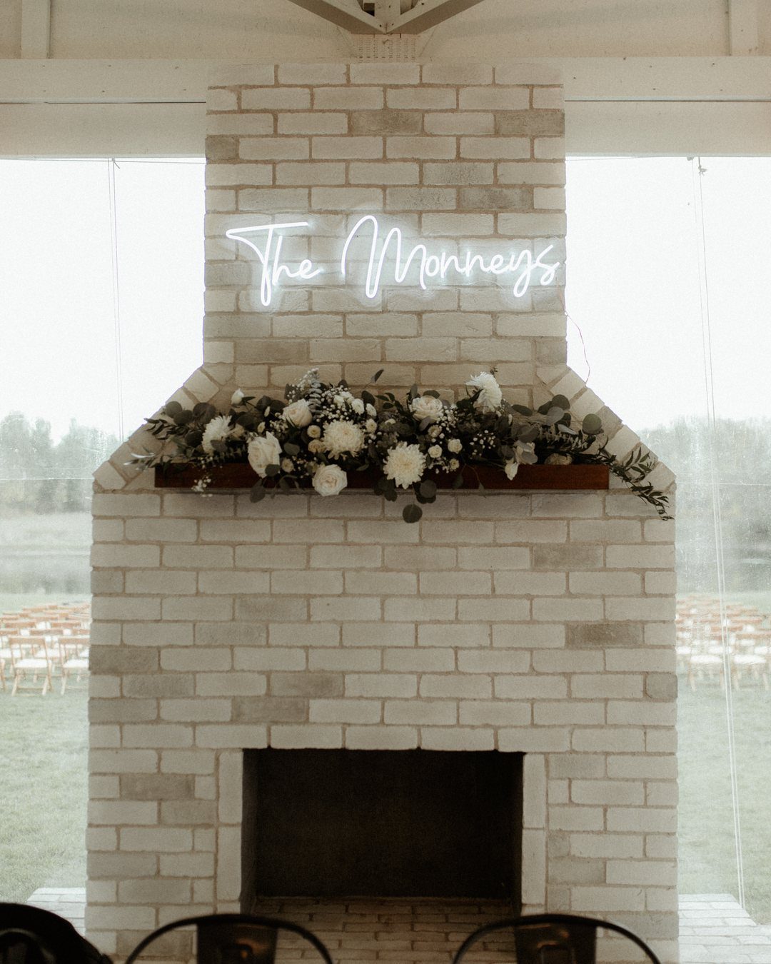 Brick fireplace with white neon sign and floral arrangement as a wedding backdrop