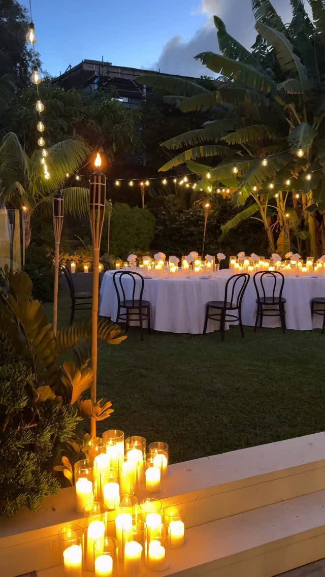 Outdoor wedding reception table with white linens, candles, and string lights in a garden