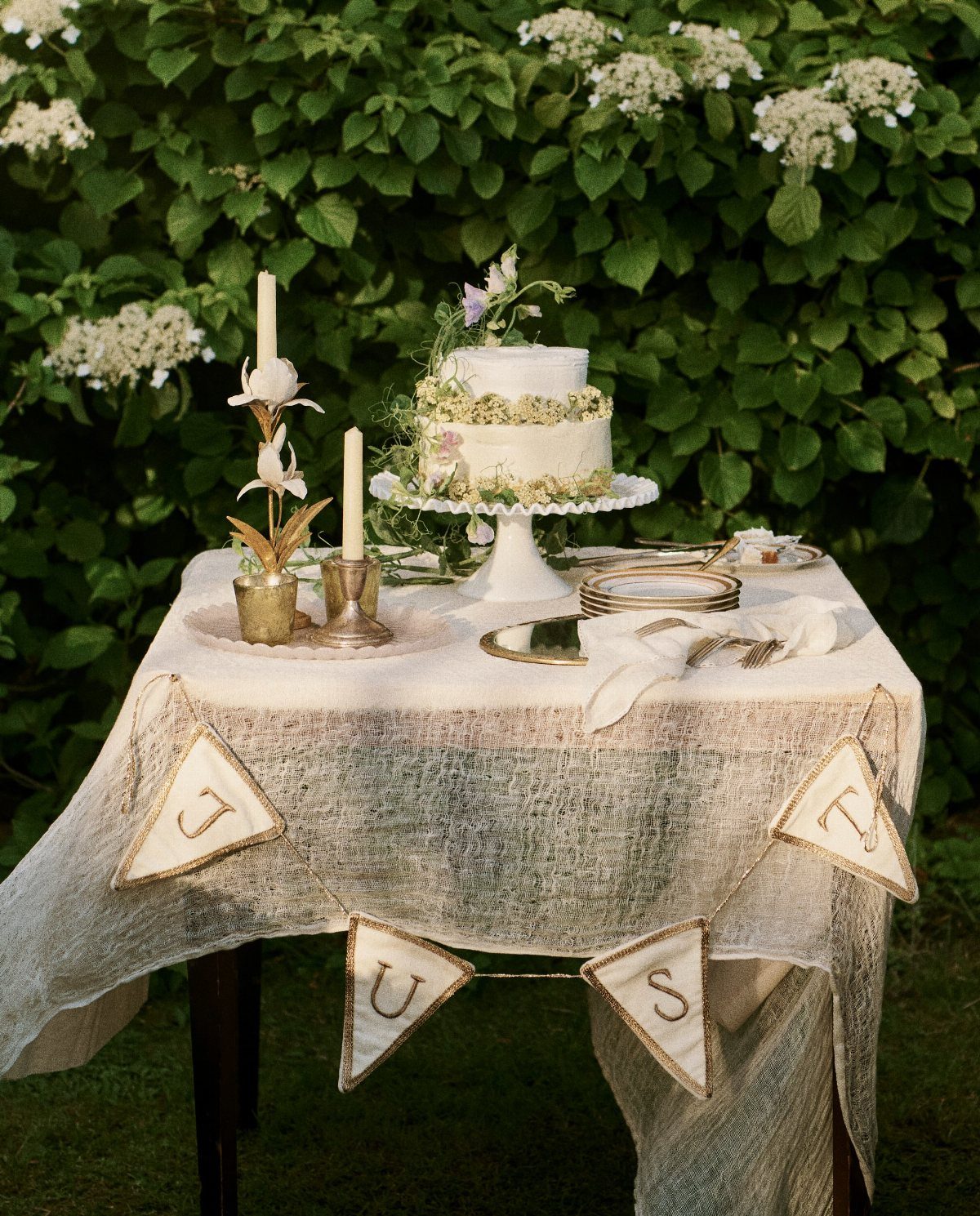 Two-tier wedding cake with floral decorations on a lace-covered table in a garden.