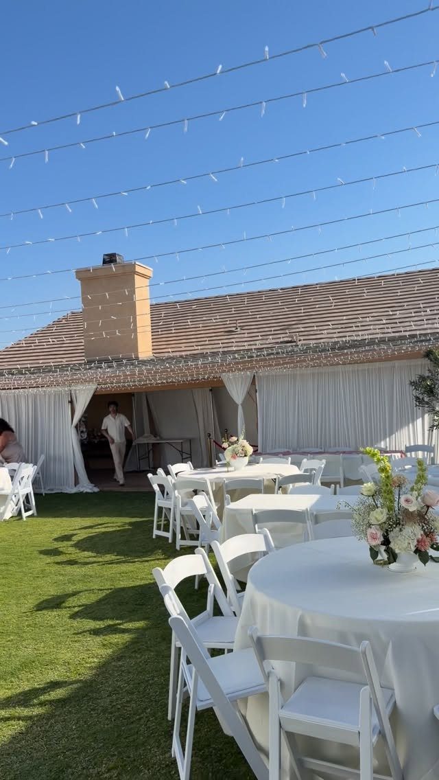 White wedding tables and chairs on a lawn under overhead string lights.