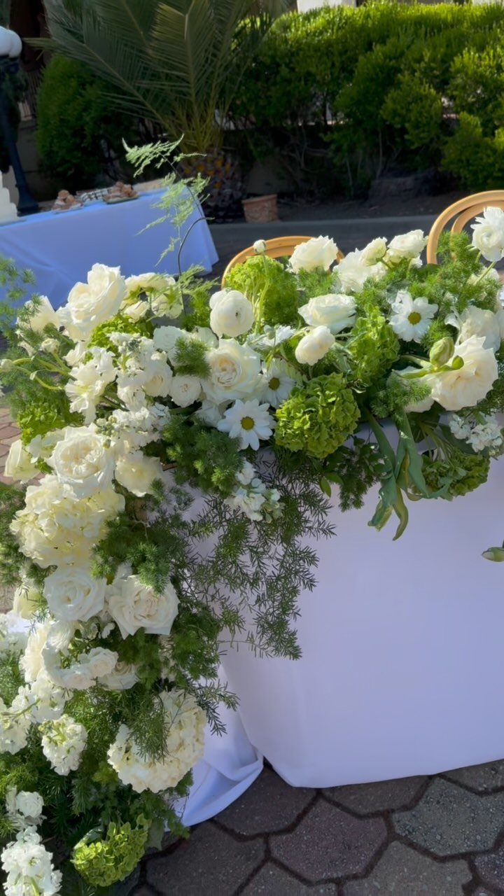 White floral arrangement with roses and greenery cascading down a white draped table.