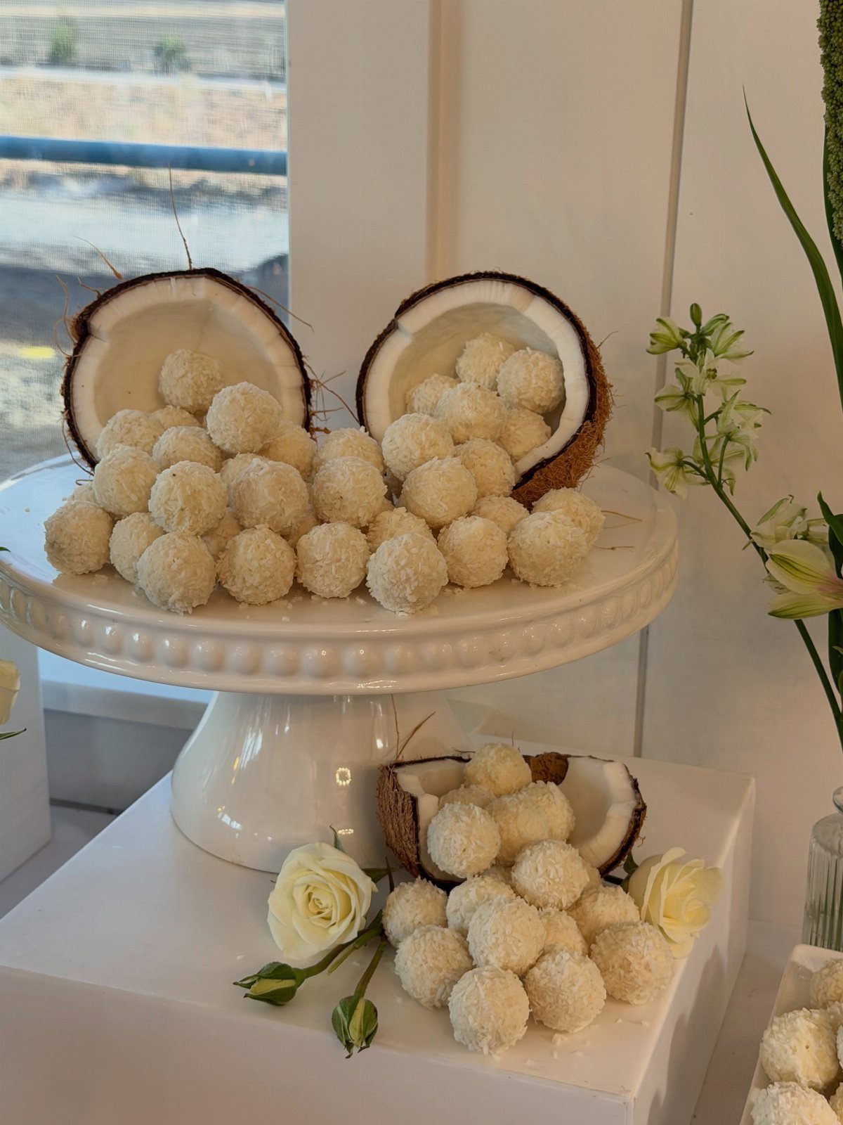 Coconut truffle balls on a white cake stand with coconut shells and roses.