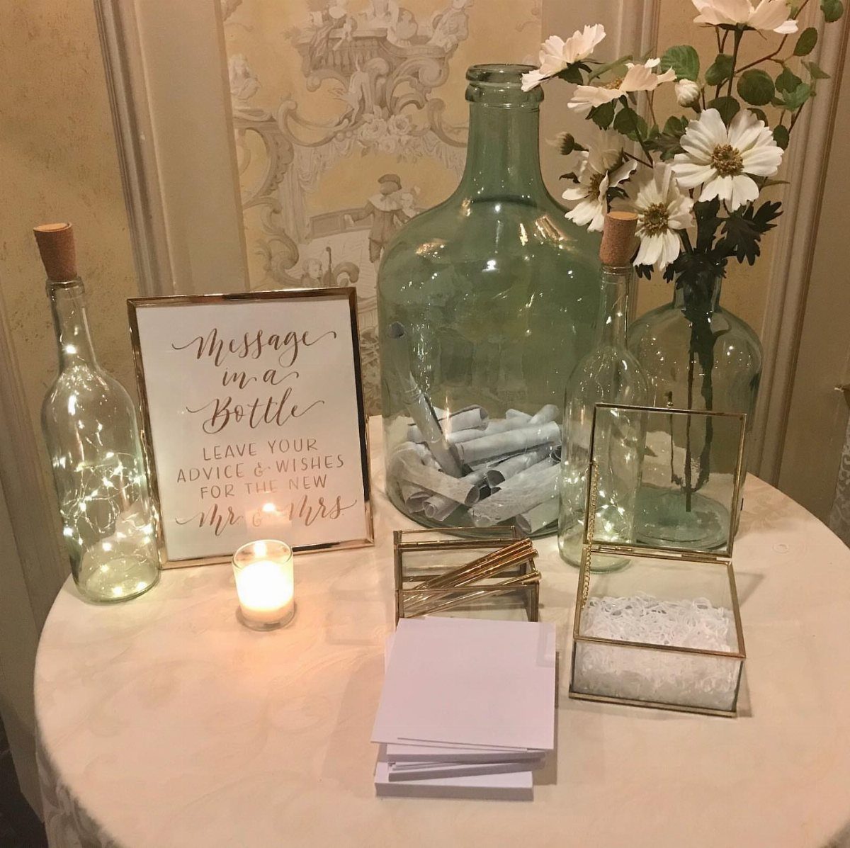 Message in a bottle wedding guest book station with glass bottles and white flowers.