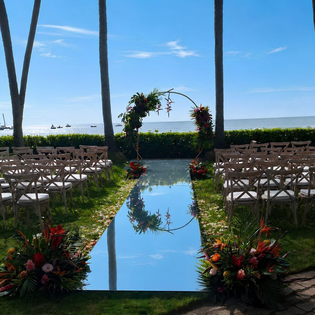 Reflective blue mirrored wedding aisle with tropical floral arrangements and a floral arch.