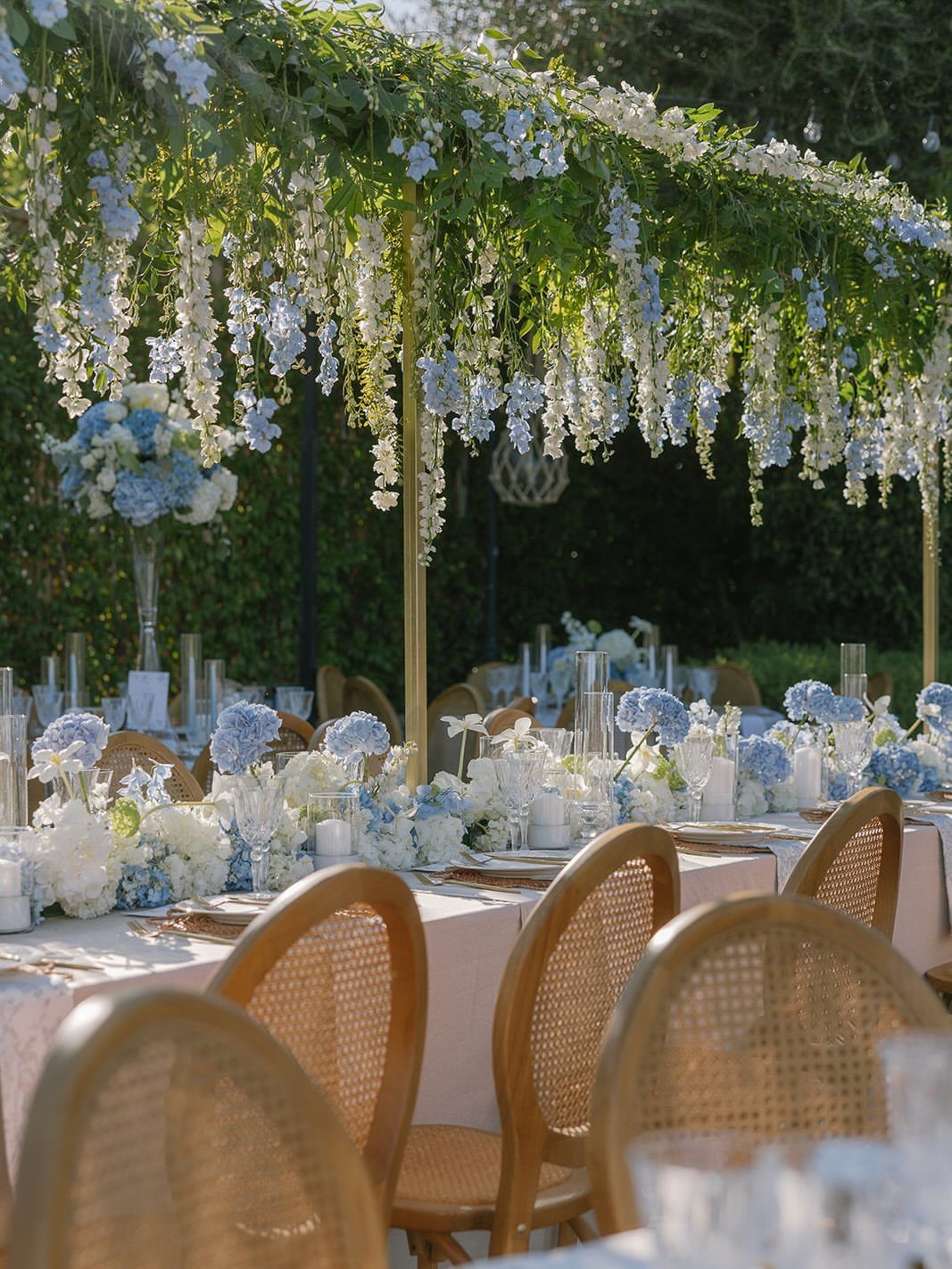 Wedding table with blue and white flowers under a floral canopy and cane chairs.