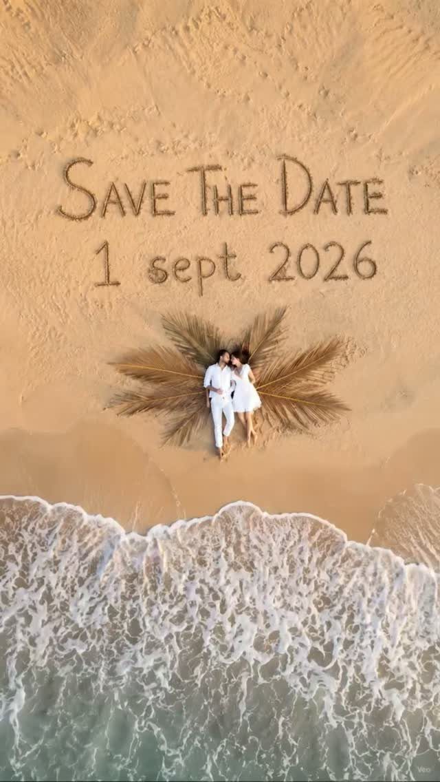 Couple in white lying on sand with Save the Date written around them.