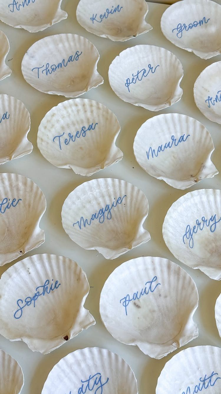 White scallop seashells with guest names written in blue cursive calligraphy for seating.