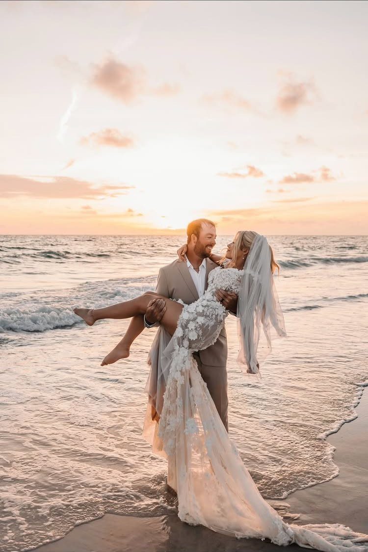 Groom carrying bride on a beach during a golden sunset wedding ceremony.