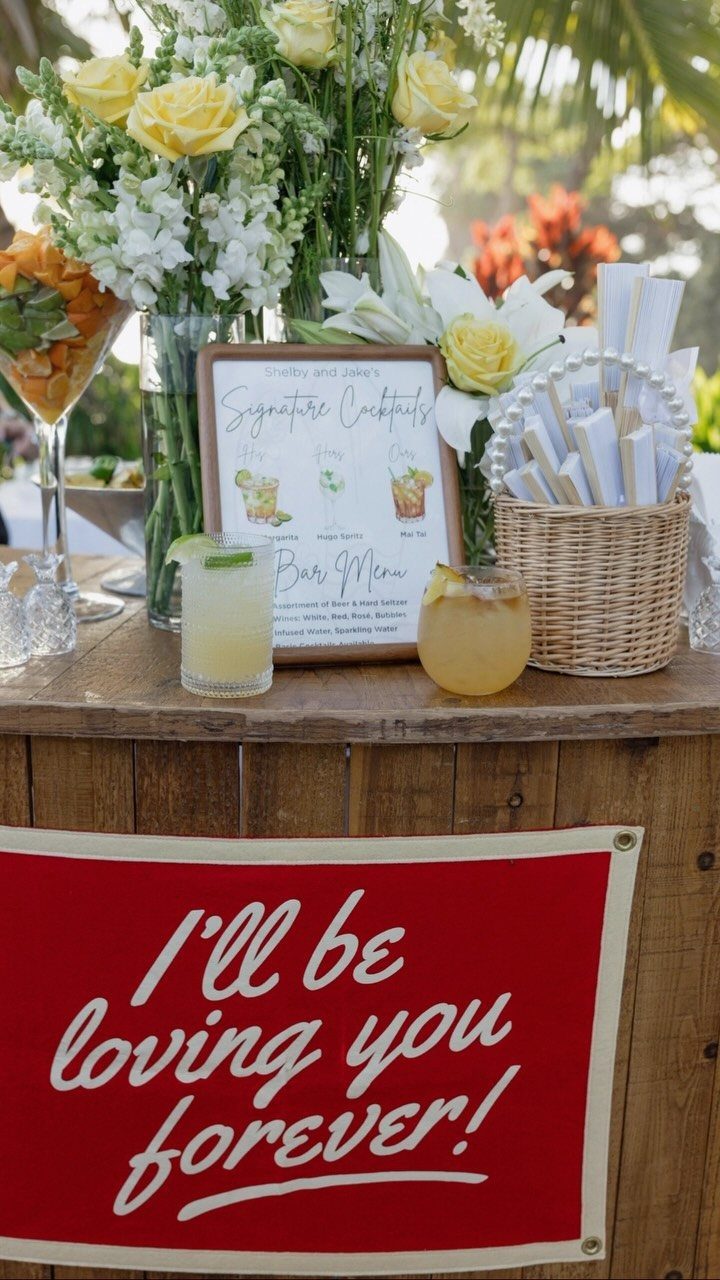 Yellow tropical cocktails on a wooden bar with a signature drinks menu and flowers.