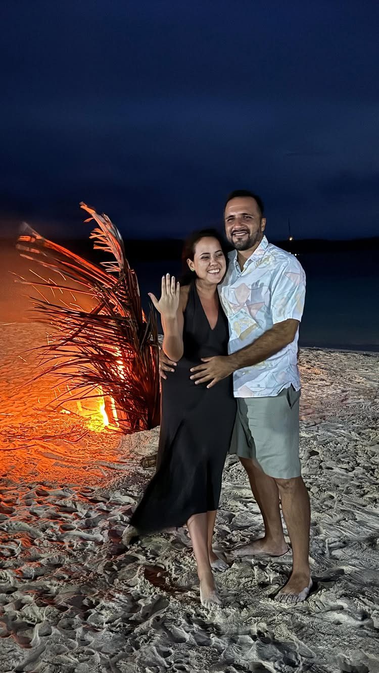 Smiling couple posing on a beach at night next to a large bonfire.