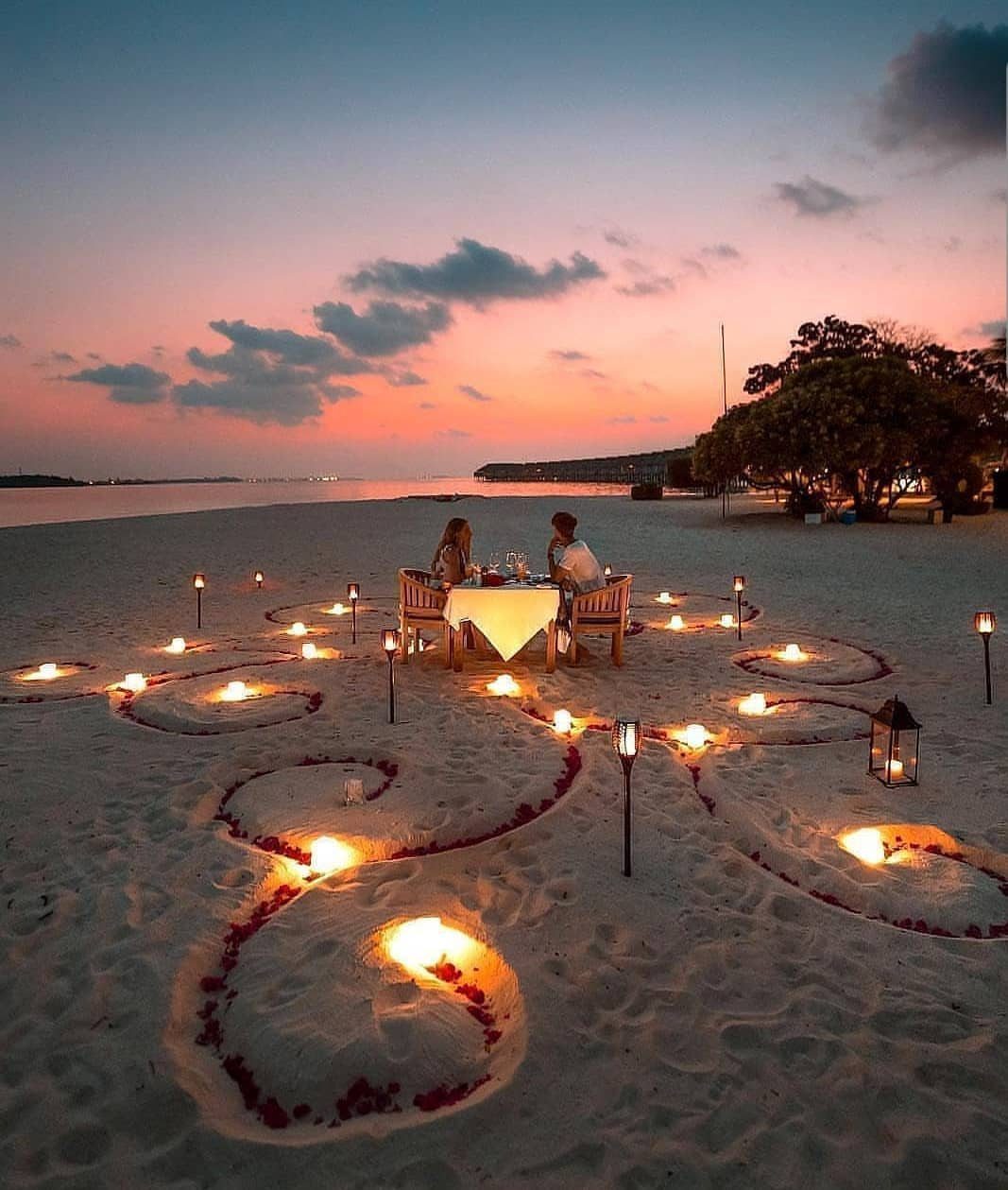 Couple dining at a romantic beach table surrounded by lanterns and flower petals.