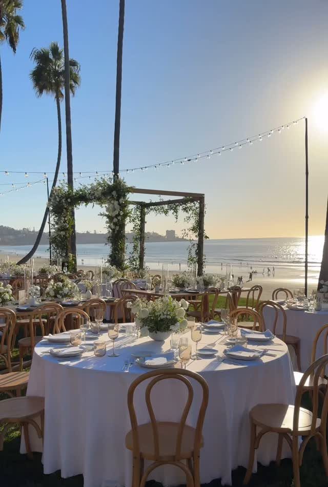 Wedding reception tables with white linens and floral centerpieces overlooking a sunny beach.