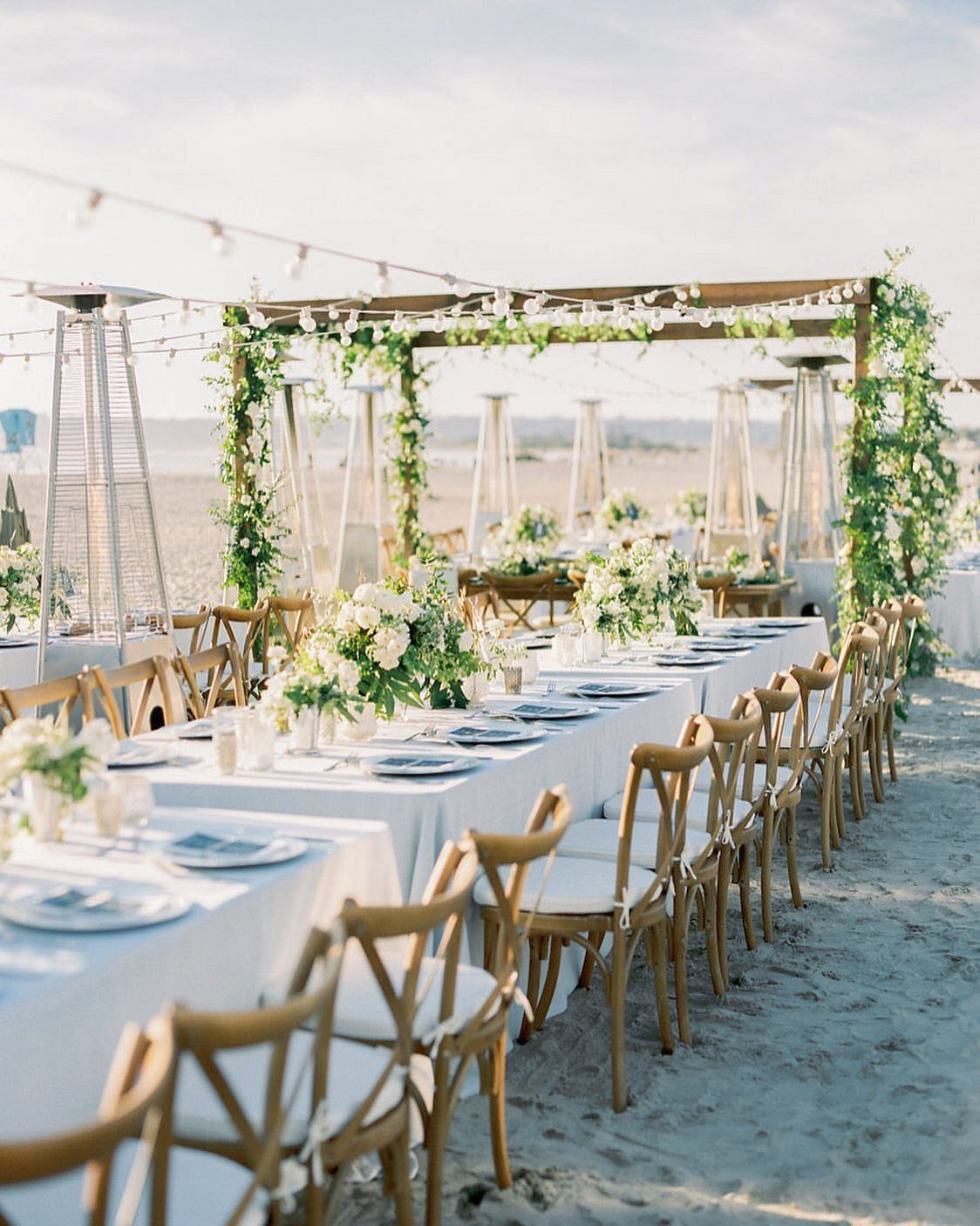 Wedding reception table with white flowers and wooden chairs on a sandy beach