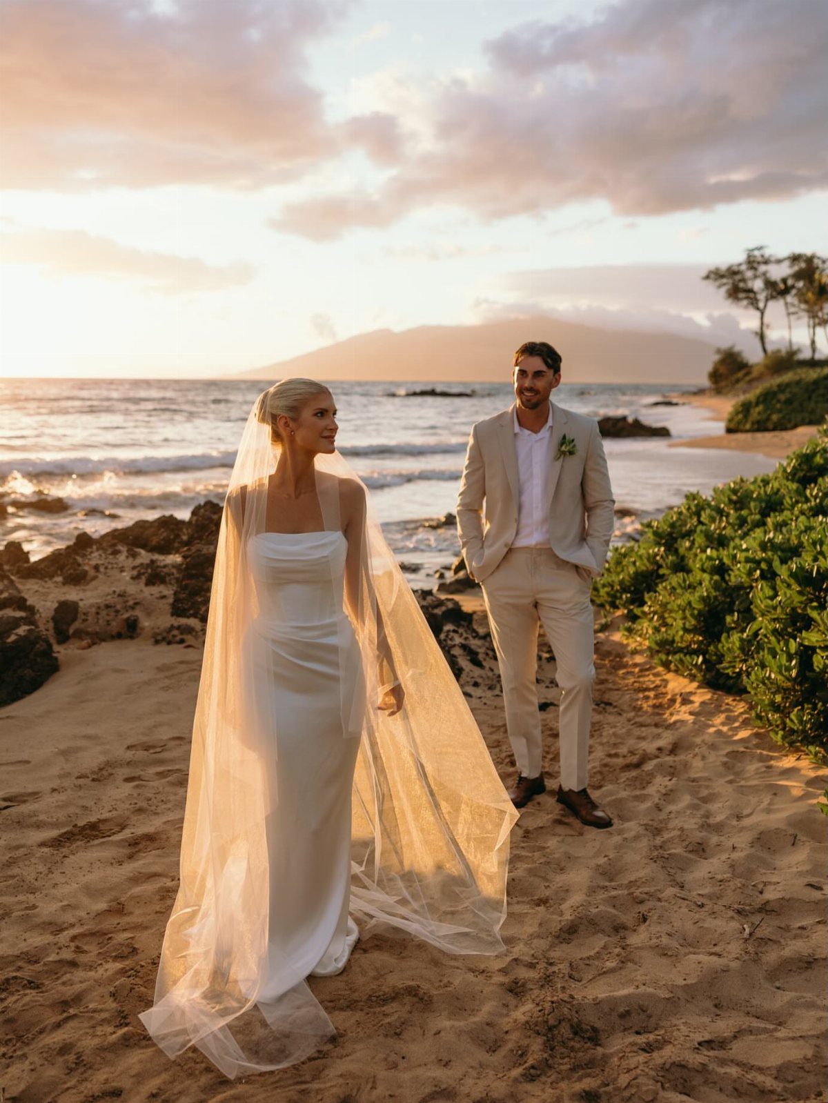 Bride and groom posing on a sandy beach during a golden hour sunset.