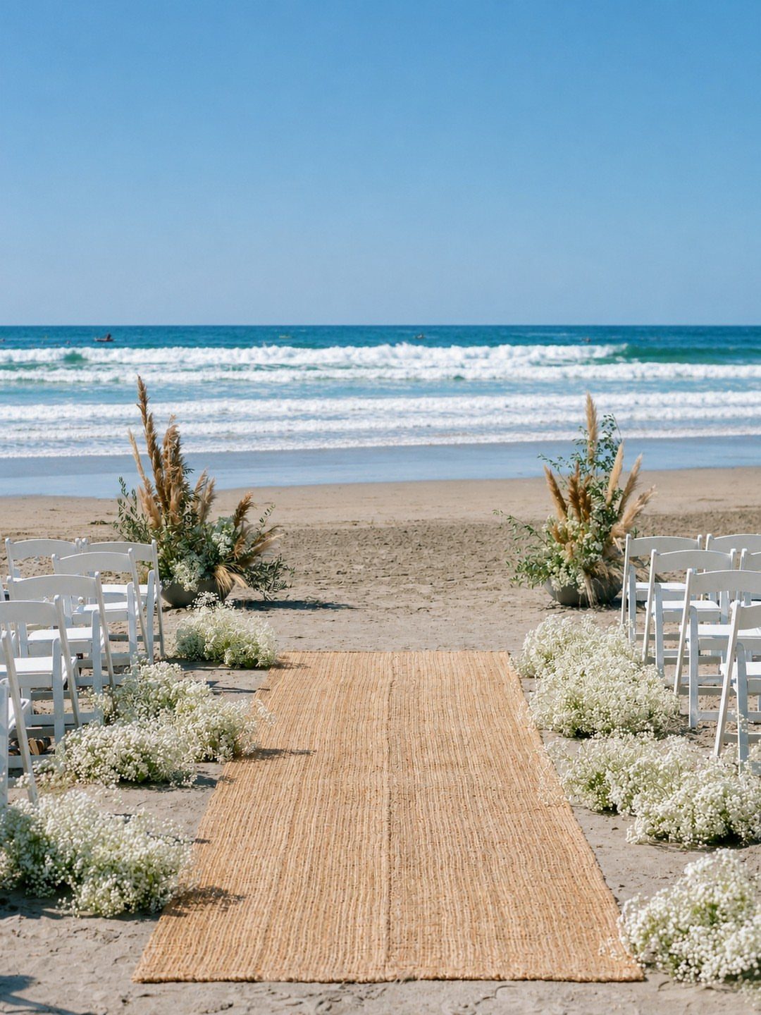 Beach wedding ceremony setup with woven aisle runner, white chairs, and ocean backdrop.